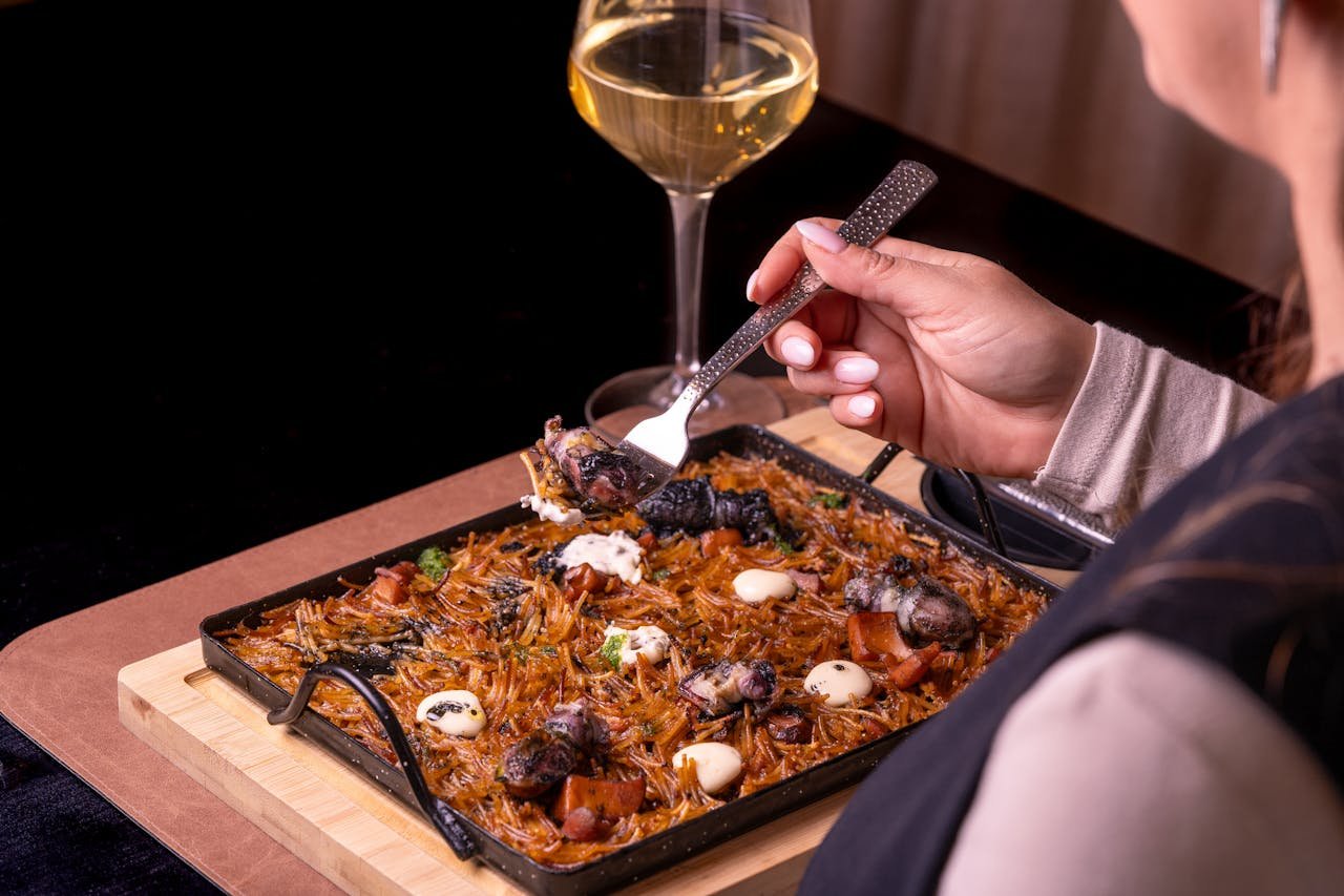 A person enjoys a delicious seafood dish paired with white wine, creating an elegant dining experience.